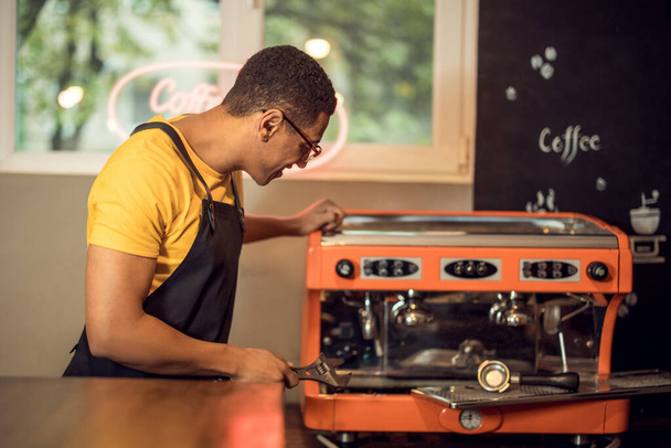 Waist-up portrait of a focused technician with a spanner in the hand looking at the coffee machine - Zdjęcie, obraz