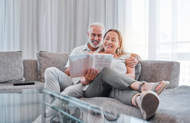 Senior couple reading book on sofa together enjoying weekend, freedom and retirement at home. Love, relaxation and mature man and woman read novel bonding, smiling and sitting on couch in living room. - Foto, imagen