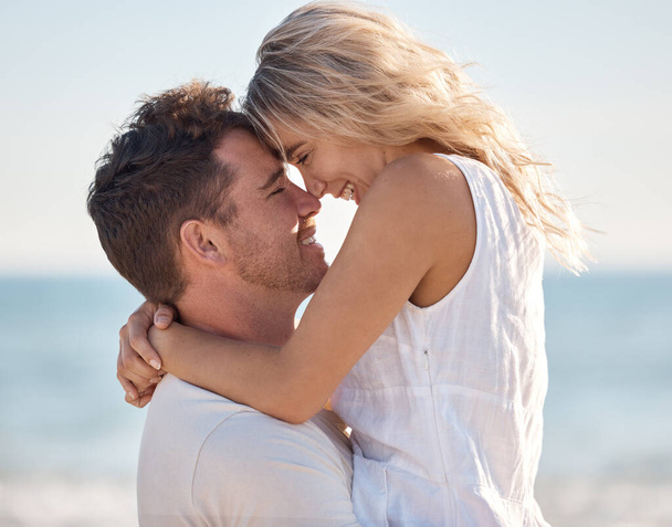 Пляж, любовь и соприкосновение носа пары с улыбкой для романтики, связи и счастья с ношением объятий. Партнер, отдых и Канадский океан обнимают летом счастливую, расслабляющую и интимную память - Фото, изображение