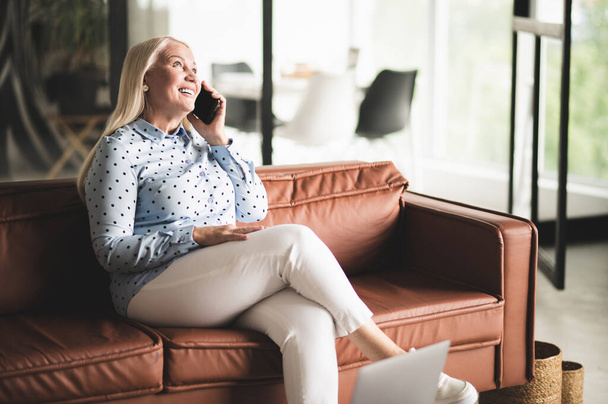 Phone call. Blonde mature woman talking on the phone while sitting on the sofa - Fotoğraf, Görsel