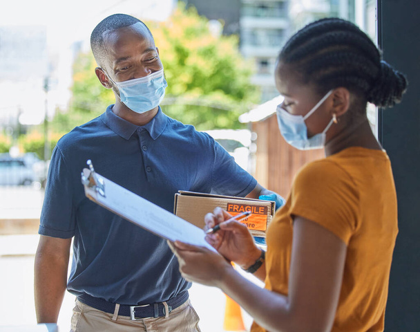 Sign, covid and black woman with a delivery at the door with a happy delivery man in a face mask for safety compliance. Ecommerce, coronavirus and African girl customer with a clipboard for a box. - Photo, Image