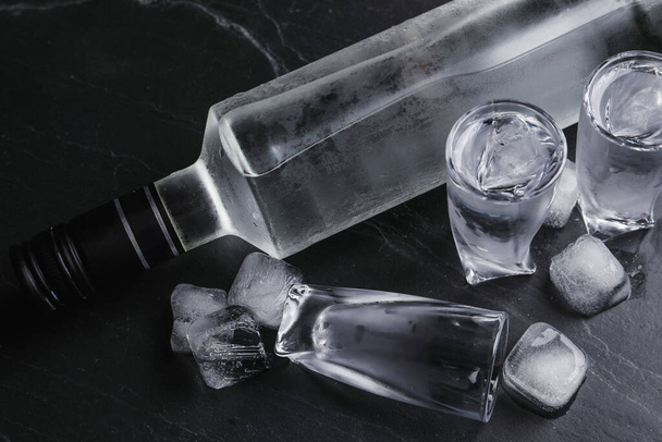 Bottle of vodka and shot glasses with ice on black table, above view - Φωτογραφία, εικόνα