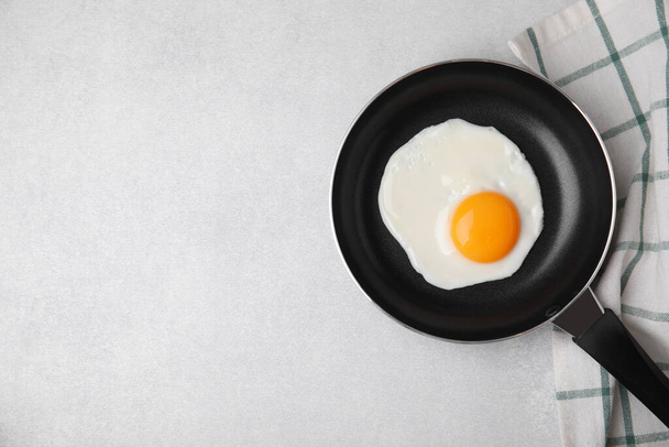 Tasty fried egg in pan on light grey table, flat lay. Space for text - 写真・画像