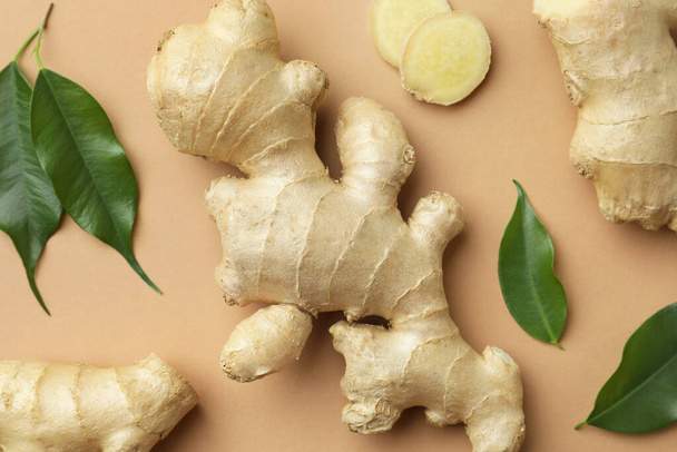 Fresh ginger with green leaves on light pale brown background, flat lay - Φωτογραφία, εικόνα