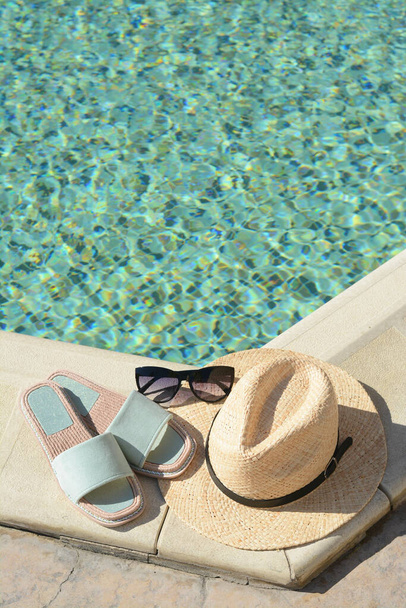 Stylish sunglasses, slippers and straw hat at poolside on sunny day, space for text. Beach accessories - Fotografie, Obrázek