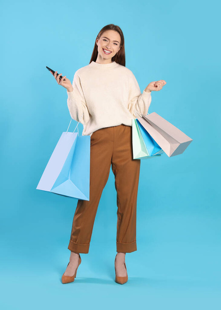 Happy young woman with shopping bags and smartphone on light blue background. Big sale - Photo, Image