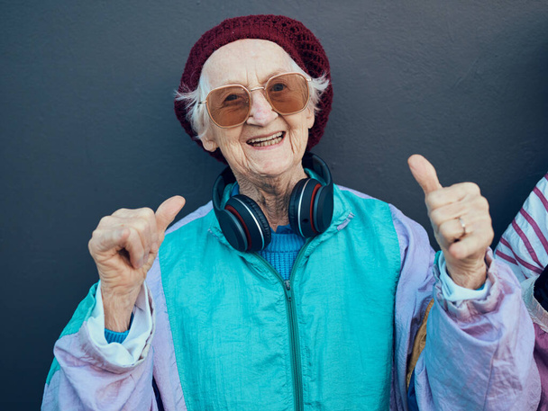 Femme âgée, pouces levés et écouteurs pour la mode élégante, lunettes ou style de vie moderne et la liberté de bonheur. Oui, mains et musique en streaming ou portrait d'une personne âgée heureuse et funky avec le sourire. - Photo, image