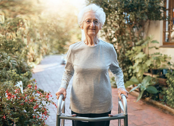 Αναπηρία, αποκατάσταση και ηλικιωμένη γυναίκα με πλαίσιο περιπάτου για εξωτερική ευεξία, κινούμενο σώμα και υγειονομική περίθαλψη στη φύση, κήπο ή πάρκο. Συνταξιοδοτικό σπίτι, φροντίδα ηλικιωμένων και πορτρέτο γριάς στο περπάτημα. - Φωτογραφία, εικόνα