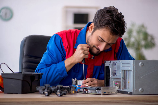 Молодой ремонтник ремонтирует компьютеры в мастерской - Фото, изображение