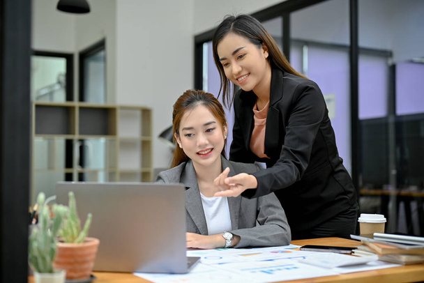 Professionelle und fröhliche asiatische Managerinnen coachen, schulen und beraten ihre jungen Mitarbeiterinnen bei der Arbeit am Laptop. - Foto, Bild