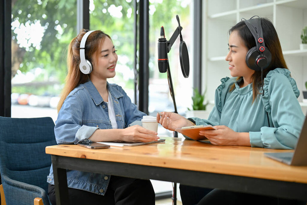 二つの魅力的な若いアジアの女性のラジオホスト彼らのオンラインラジオ番組やポッドキャストを一緒にスタジオで実行. - 写真・画像