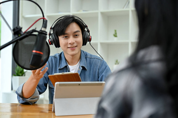 Профессиональный и талантливый молодой азиатский радиоведущий-мужчина наслаждается обсуждением и интервью со своей специальной гостьей во время подкаста шоу в студии. - Фото, изображение