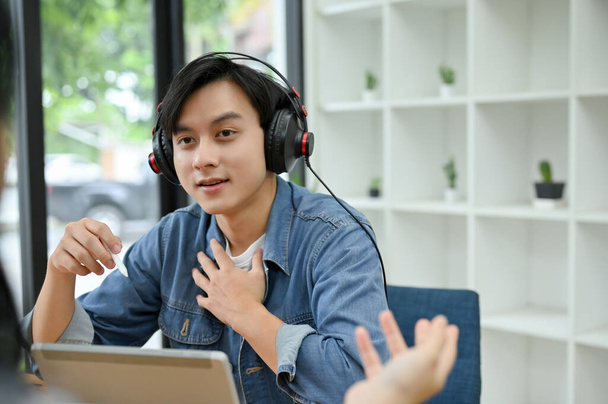 Viehättävä ja lahjakas nuori aasialainen miespuolinen radiojuontaja puhuu ja haastattelee vierastaan studiossa.. - Valokuva, kuva