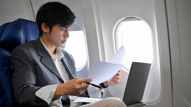Ocupado e inteligente joven empresario asiático o gerente ejecutivo masculino trabajando y comprobando su papeleo de negocios durante el vuelo en su jet privado. - Foto, Imagen