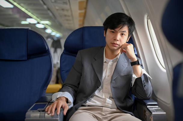 Guapo e inteligente joven empresario asiático o jefe de negocios en traje formal se sienta en el asiento de la ventana en una clase de negocios. Concepto de transporte aéreo - Foto, imagen