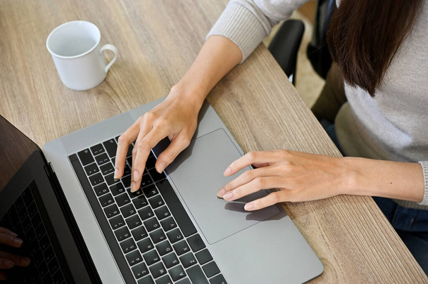 Eine Unternehmerin oder Freiberuflerin, die am Laptop arbeitet, auf der Tastatur tippt, im Internet surft und an ihren Online-Aufgaben arbeitet. Ansicht von oben, Nahaufnahme der Hände - Foto, Bild