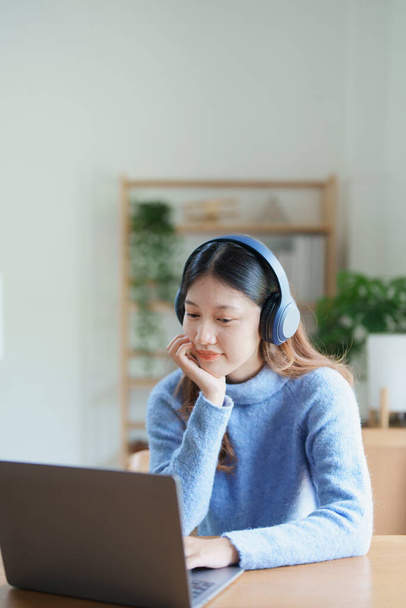 Muotokuva teini-ikäinen aasialainen nainen käyttää tietokonetta, yllään kuulokkeet opiskella verkossa kautta videoneuvottelut puinen työpöytä kotona. - Valokuva, kuva