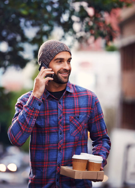 Kávét hozok. Egy jóképű fiatalember télen mobilon beszél, miközben kávét tart a kezében. - Fotó, kép
