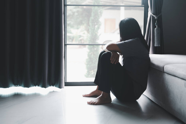 Schizophrénie avec solitaire et triste en santé mentale concept de dépression. Femme déprimée assise contre le sol à la maison avec chambre sombre se sentant malheureux. Les femmes sont déprimées, effrayées et malheureuses. - Photo, image