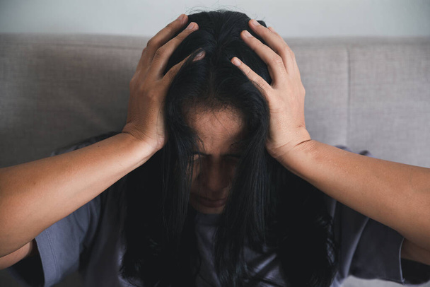 Schizophrenia with lonely and sad in mental health depression concept. Depressed woman sitting against on the sofa at home with dark room feeling miserable. Women are depressed, fearful and unhappy. - Photo, image