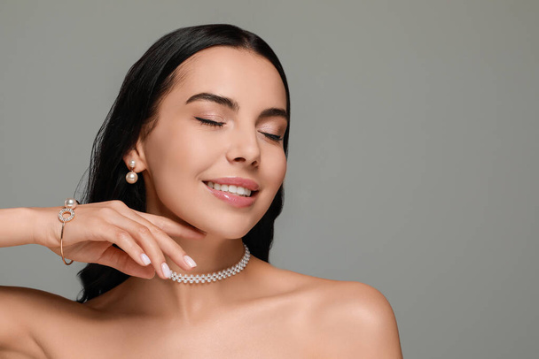 Young woman wearing elegant pearl jewelry on grey background, space for text - Fotoğraf, Görsel