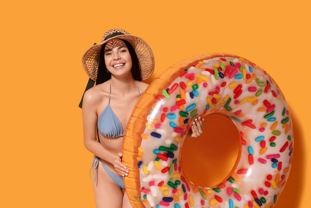 Young woman with straw hat holding inflatable ring against orange background - Fotografie, Obrázek