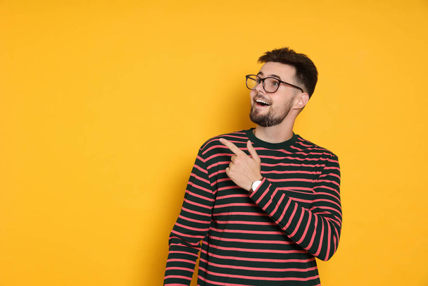 Handsome man in striped sweatshirt pointing at something on yellow background, space for text - Zdjęcie, obraz