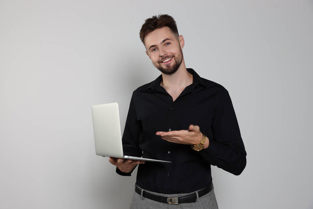 Handsome man in black shirt working with laptop on light grey background - Foto, afbeelding