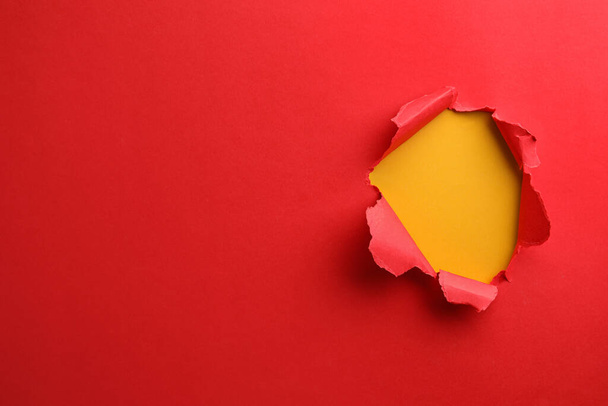 Hole in red paper on yellow background, space for text - Valokuva, kuva