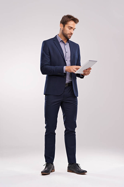 Revisando las últimas actualizaciones. Captura de estudio de un hombre bien vestido usando una tableta sobre un fondo gris - Foto, Imagen