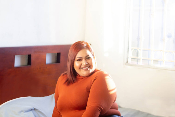 joven modelo de talla grande sonriendo sentada en su cama. mujer mexicana con sobrepeso - Foto, imagen