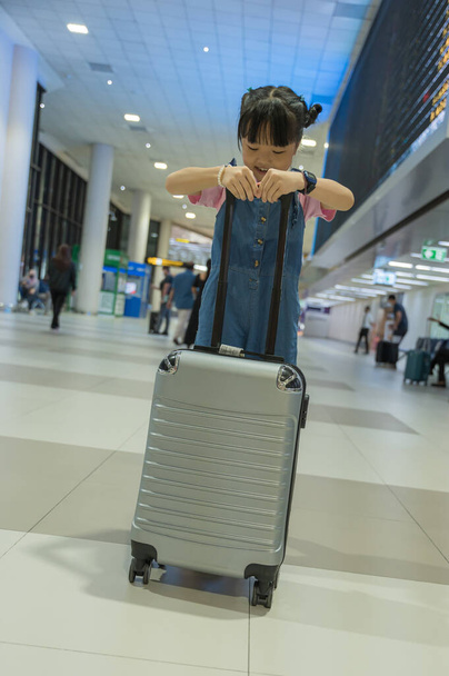 Linda niña feliz con maleta en la terminal del aeropuerto. Niño y familia viajando de vacaciones para esperar el embarque en la terminal. Concepto de viaje familiar. - Foto, imagen