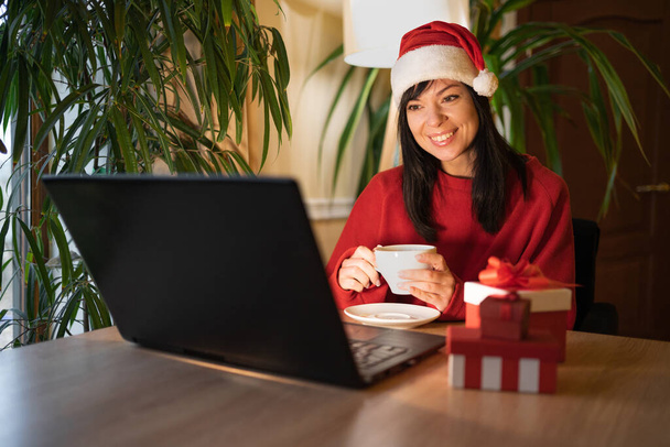 Dizüstü bilgisayarda film izleyen gülümseyen genç bir kadın Noel arifesinde akşam çayı içerken gülümsüyor. Boşluğu kopyala - Fotoğraf, Görsel