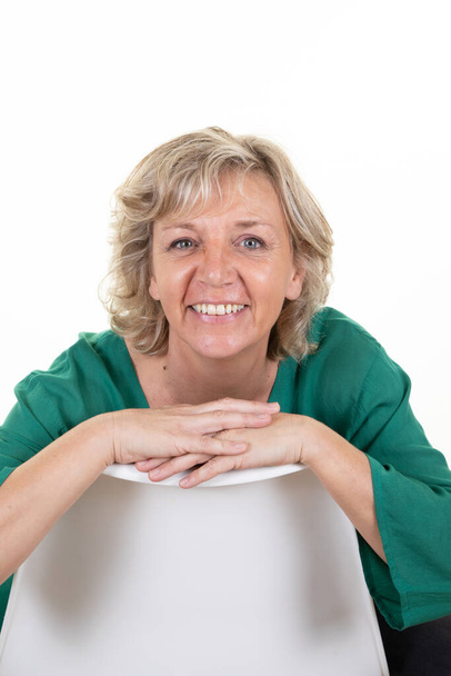 souriant mignon mature femme senior blond assis sur fond blanc - Photo, image