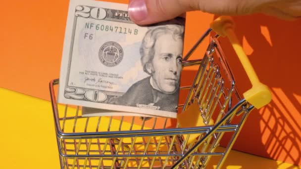 Sarı arka planda oyuncak süpermarket tramvayına 20 dolarlık banknot ekle. Amerikan dolarlarının sepetini satıyor. Asgari yaşam maaşı kavramı: kredi, yatırım emekliliği tasarrufu - Video, Çekim