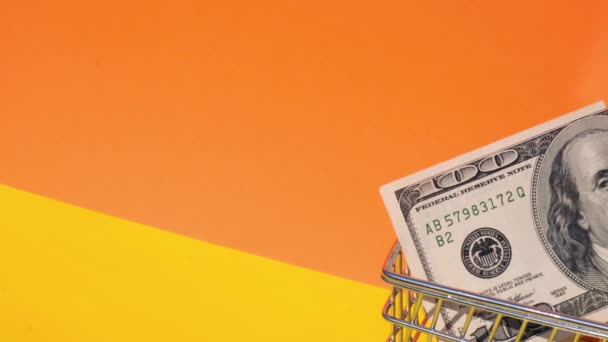 Handschiebender Supermarkt-Einkaufswagen mit 100-Dollar-Schein Geld im Einkaufswagen auf gelbem Hintergrund. Verkaufskorb von US-Dollar-Scheinen. Existenzminimumkonzept: Darlehen, Altersvorsorge ansparen - Filmmaterial, Video