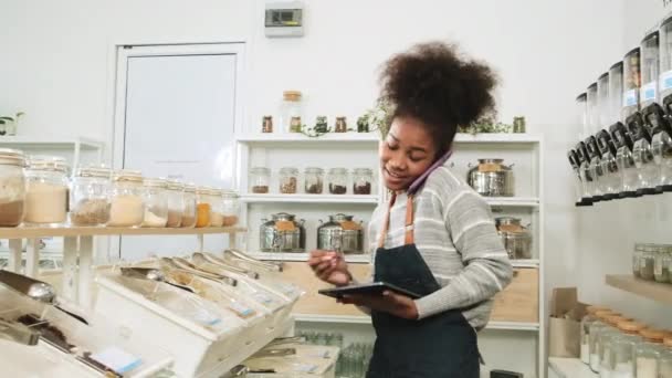 Eine schwarze Ladenbesitzerin arbeitet im Refill-Store, telefoniert mit Kunden und überprüft Lagerbestellungen von Bioprodukten in Mehrwegcontainern, einem Null-Abfall-Lebensmittelladen und nachhaltigem Wirtschaften. - Filmmaterial, Video