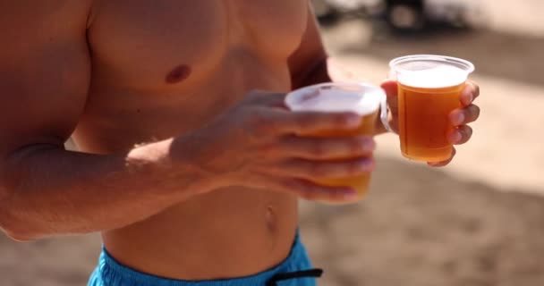 Op het strand houdt een jongeman bier in zijn handen, een close-up, slow motion. Zee vakantie, concept open grens - Video