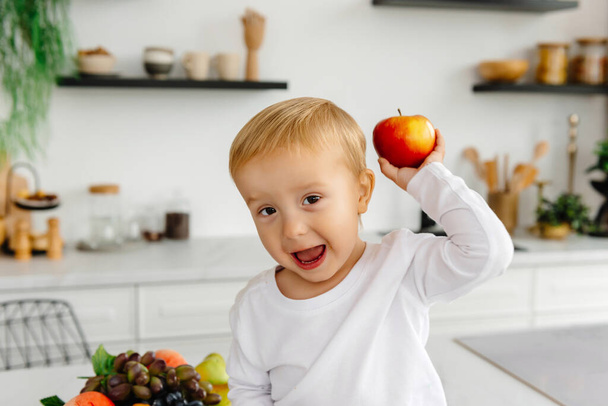 uma criança feliz segurando uma maçã vermelha na mão e acenando para a câmera. - Foto, Imagem