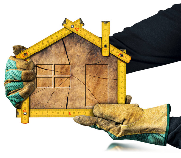 Stolarz z ochronnymi rękawicami roboczymi trzymający drewnianą, żółtą linijkę składaną w kształcie domu z przekrojem poprzecznym pnia drzewa wewnątrz, odizolowany na białym tle. - Zdjęcie, obraz