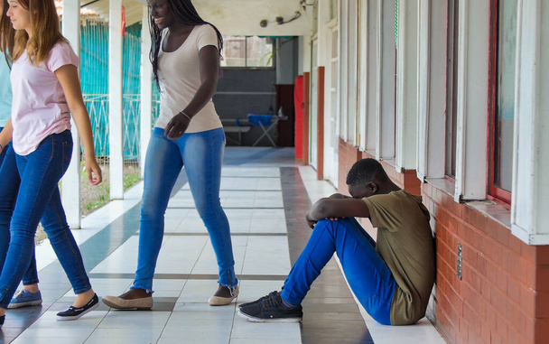 Genç çocuk okulda üzgün bir şekilde yalnız oturuyor. Depresyondaki Afrikalı çocuk koridorda terk edilmiş ve tuğla duvara yaslanmış. Zorbalık, ayrımcılık ve ırkçılık kavramı. - Fotoğraf, Görsel