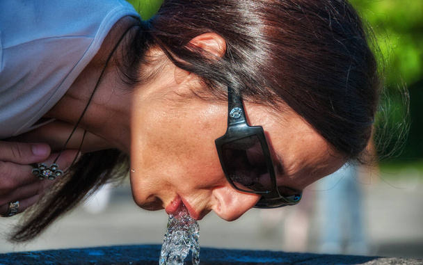 Красива коричнева жінка п'є воду з фонтану
. - Фото, зображення