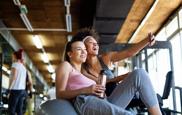Happy fit women, friends smiling, talking and taking photos after work out in gym. Social media, people, sport concept. - Fotó, kép