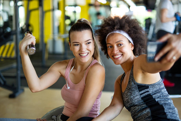 Happy fit women, friends smiling, talking and taking photos after work out in gym. Social media, people, sport concept. - Fotó, kép