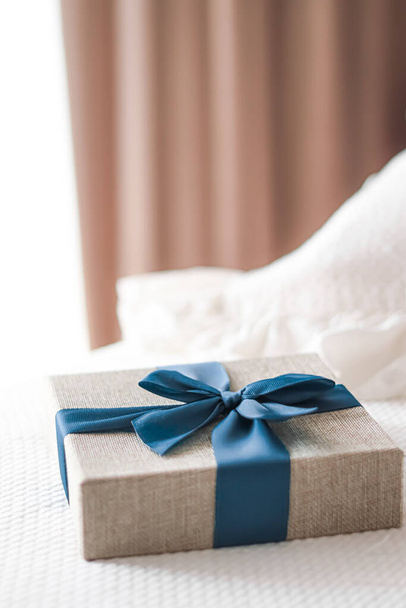 Святковий подарунок і розкішна онлайн доставка покупок, загорнута лляна подарункова коробка з синьою стрічкою на ліжку в спальні, шикарний сільський стиль, крупним планом
 - Фото, зображення