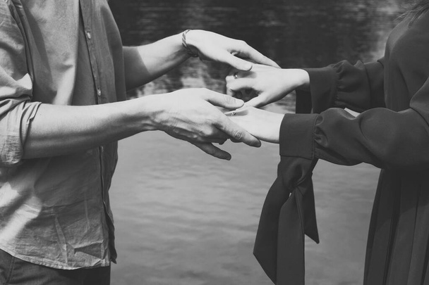 Close up partners holding hands monochrome concept photo. Romantic couple. Side view photography with lake on background. High quality picture for wallpaper, travel blog, magazine, article - Photo, Image