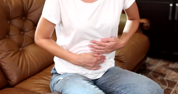 Eine Frau zu Hause auf der Couch streicht aus nächster Nähe über den Magen. Bauchschmerzen, Koliken im Darm, Zeitlupe - Filmmaterial, Video