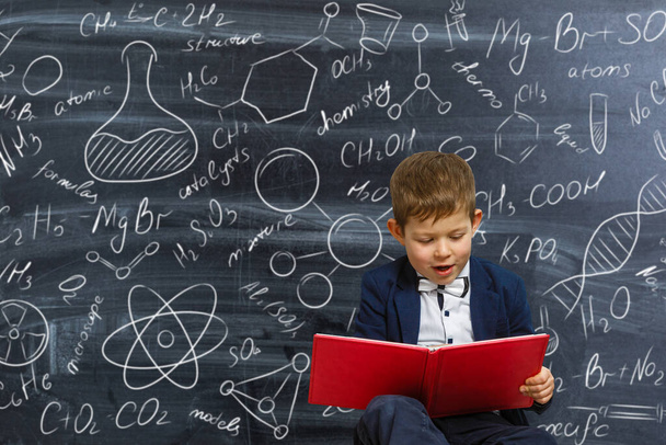 Portré egy okos kisfiú iskolai egyenruhában a háttérben egy tábla tudományos képletek és diagramok. Okos gyerekek. Oktatás - Fotó, kép