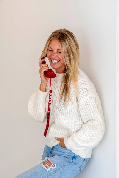 Ένα πανέμορφο ξανθό μοντέλο μιλάει στο τηλέφωνο δείχνοντας συναίσθημα σε ένα περιβάλλον σπιτιού - Φωτογραφία, εικόνα