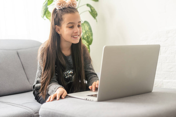 家庭でノートを作るからオンラインで勉強10代の女の子の学校の生徒。10代の学生の距離は、ノートパソコンで宿題をしたり、ビデオレッスンを見たりします。遠隔教育の概念. - 写真・画像